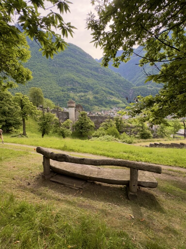 Holzbank mit Blick auf Ruine und grüne Berge im Tessin - ein Ort zum Durchatmen beim Soft Hiking.
